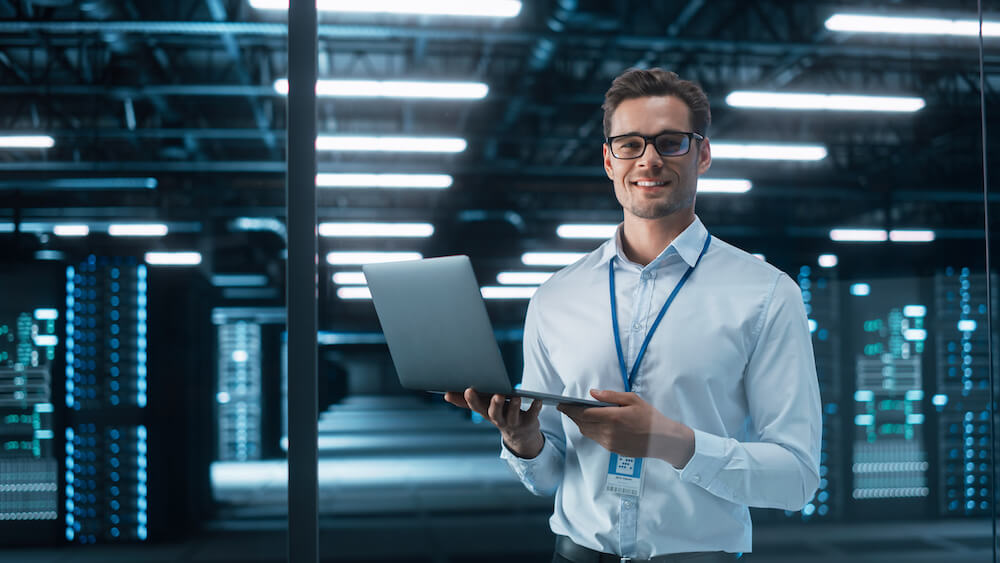 It consultant smiling at the camera while working on a report on his computer