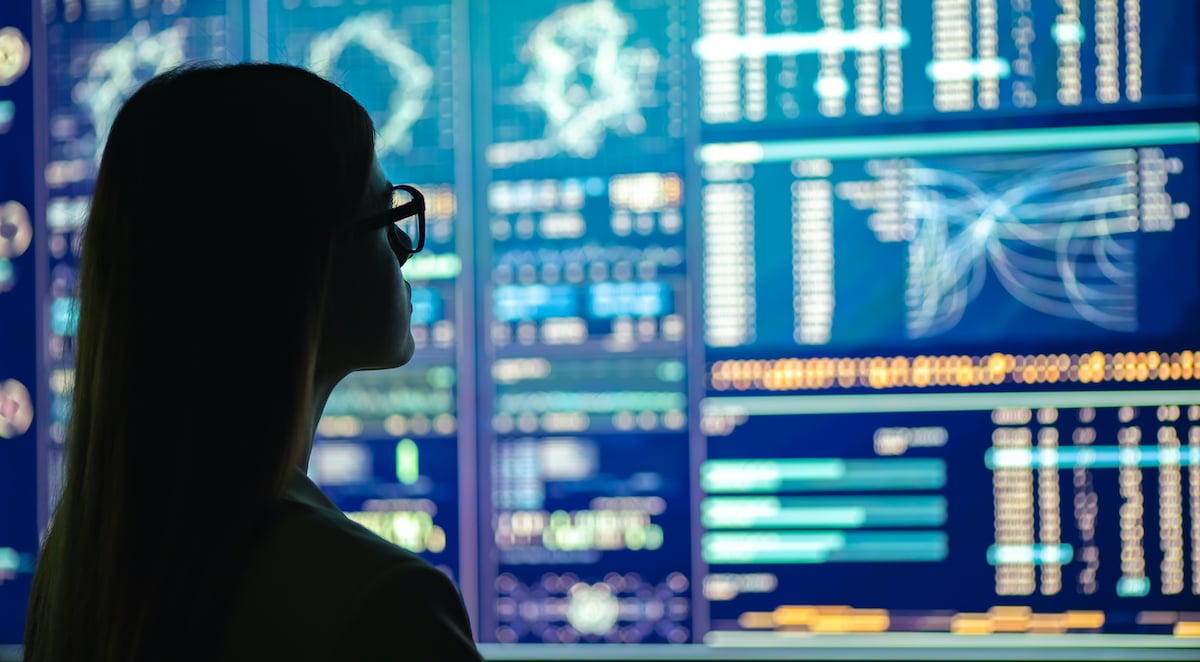 Silhouette of a woman analyzing data from a big computer in front of her