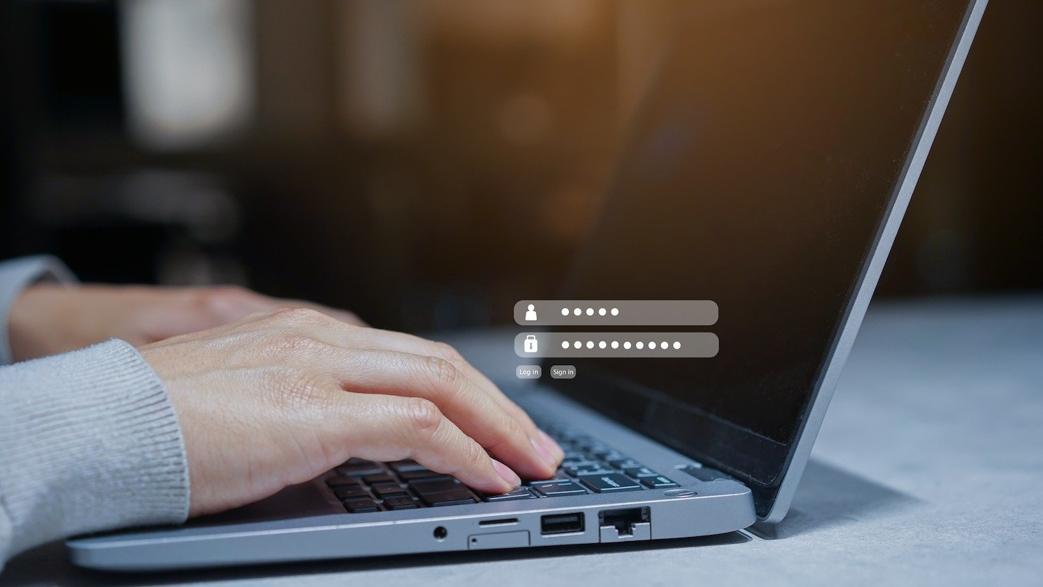 Hands typing on a laptop with visible login fields.