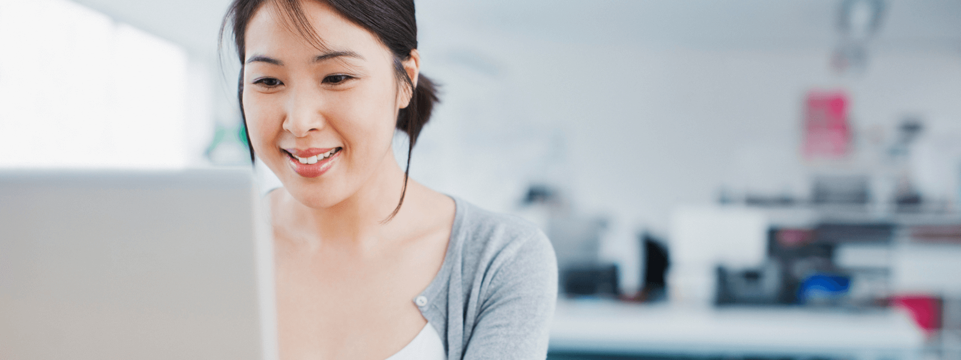 Woman sitting on a desk and smiling while checking something on her laptop