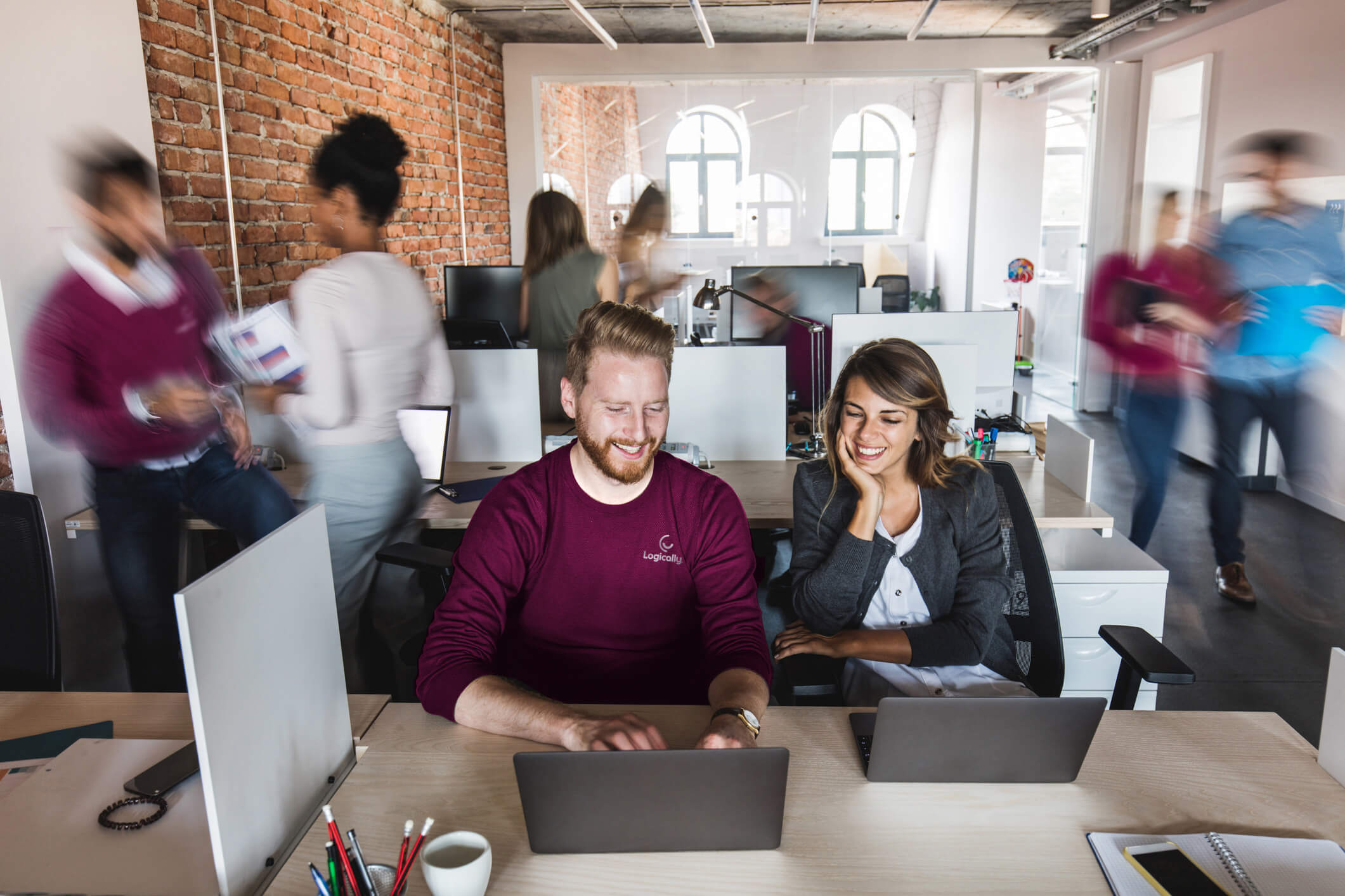 Man and woman smiling working at an office while their coworkers look blurry